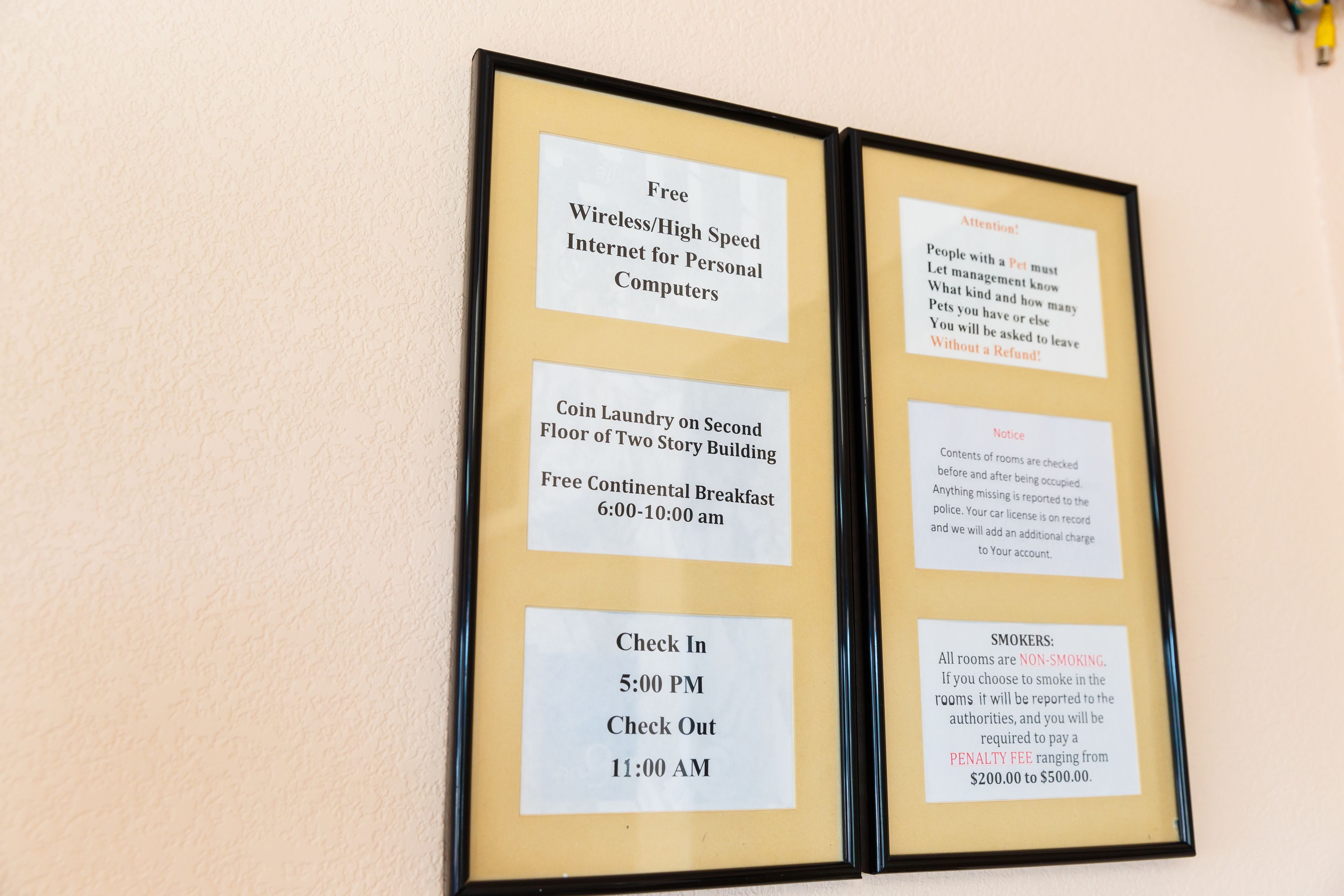 A framed sign with information about amenities and rules, including free high-speed internet, coin laundry, breakfast hours, check-in and check-out times, pet policies, smoking rules, and room checks.