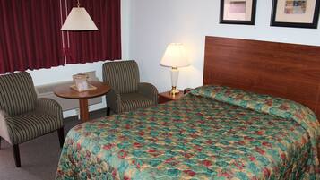 A hotel room with a bed, two chairs, a table, a lamp, and two framed pictures on the wall.