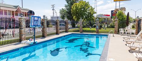 A swimming pool with a shark design, surrounded by a fence and lounge chairs.