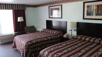 A hotel room with two beds, a heater, a lamp, and a framed picture on the wall.