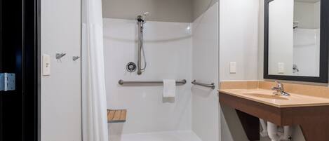 A handicap-accessible shower with a grab bar, a wooden shelf, and a sink with a mirror.