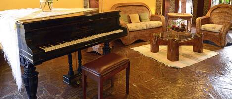 A grand piano in a cozy room with wicker furniture and a stone floor.