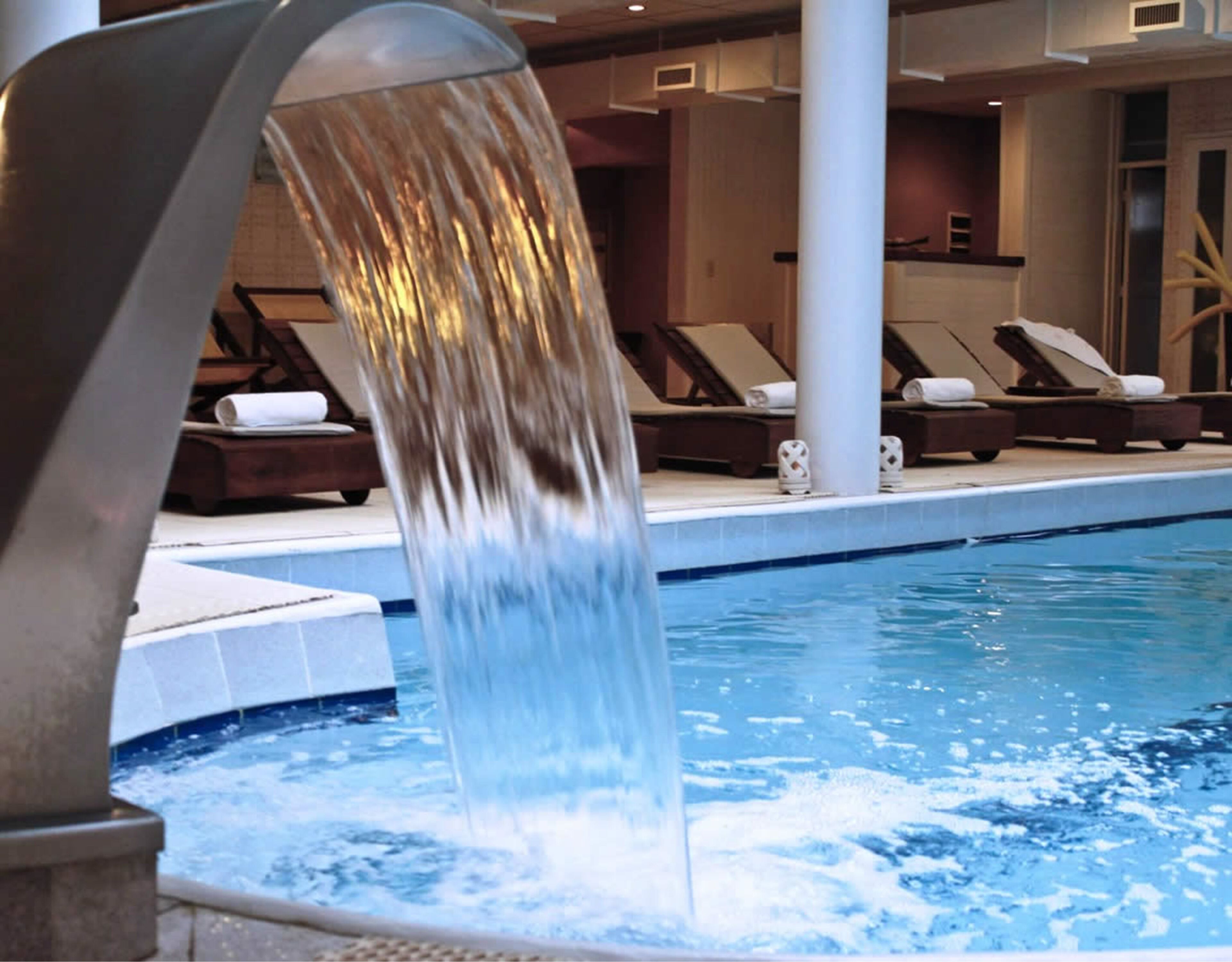 Une piscine agrémentée d’une cascade, de chaises longues et d’un espace dédié aux soins.