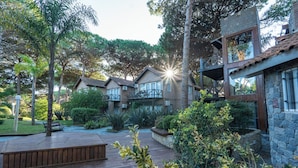 A courtyard with a wooden deck, stone walls, and a mix of trees and shrubs. - Carilo Village Apart Hotel & Spa (Carilo)