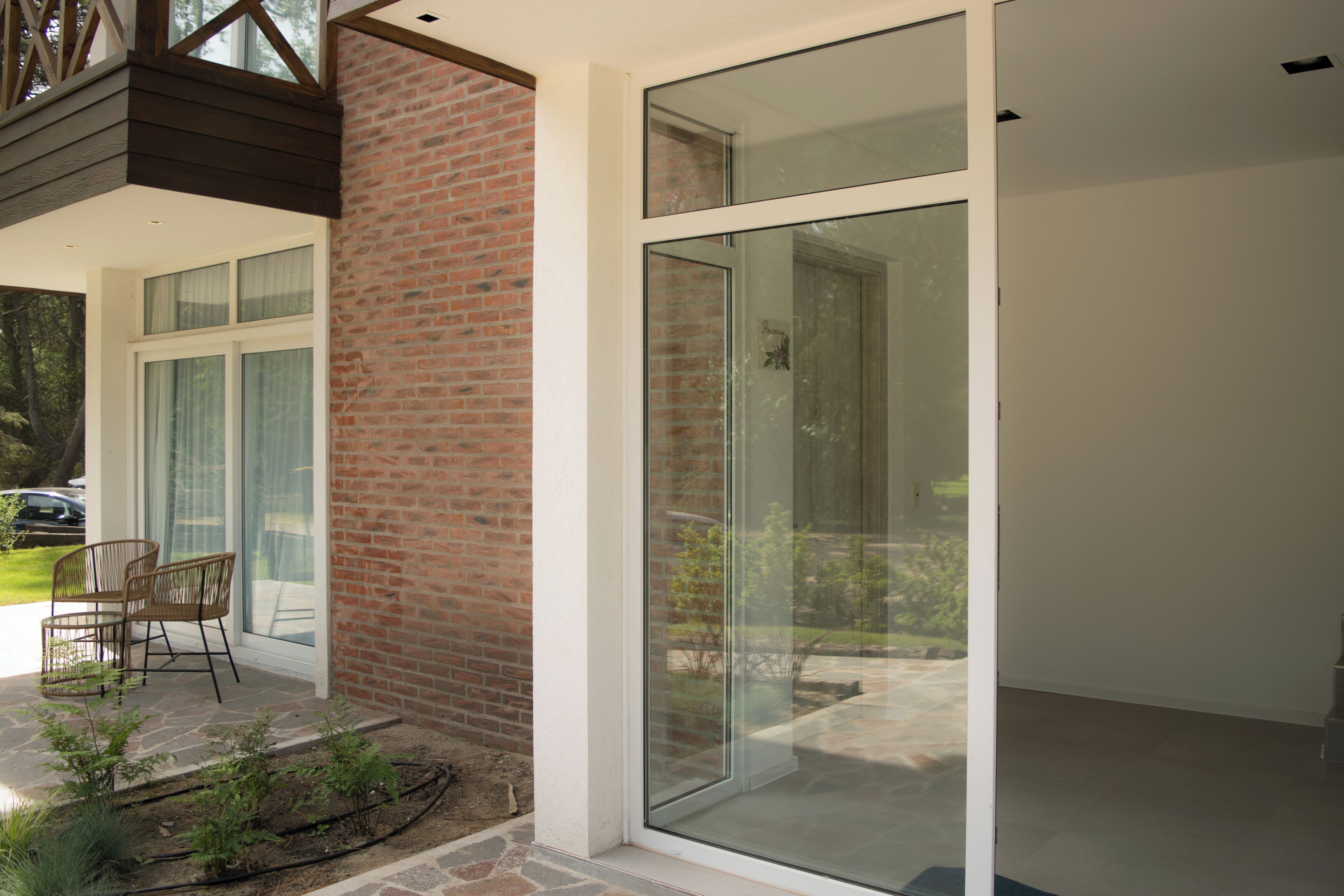 A modern house with a brick exterior, large sliding glass doors, and a patio with chairs.