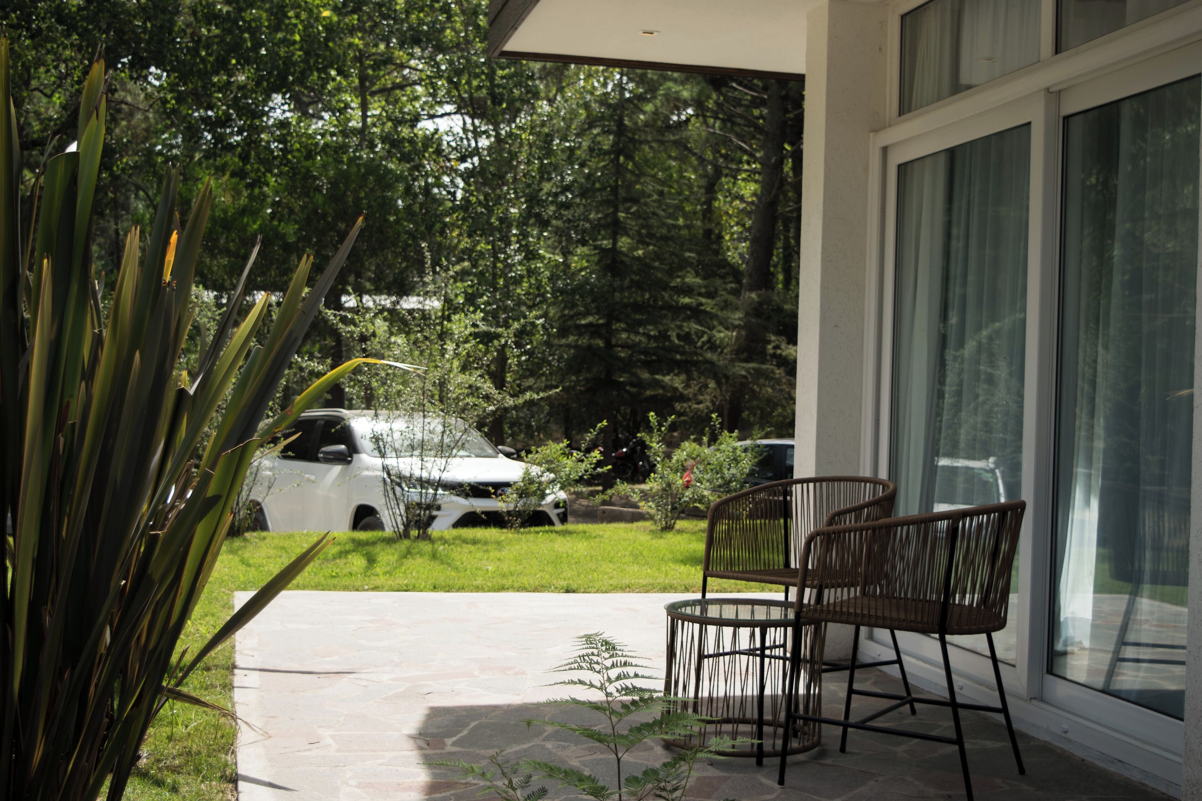 A patio with chairs, a car, and a house with a large window.