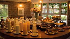 A breakfast buffet with various food items and beverages, a vase of flowers, and a brick wall with windows. - Carilo Village Apart Hotel & Spa (Carilo)