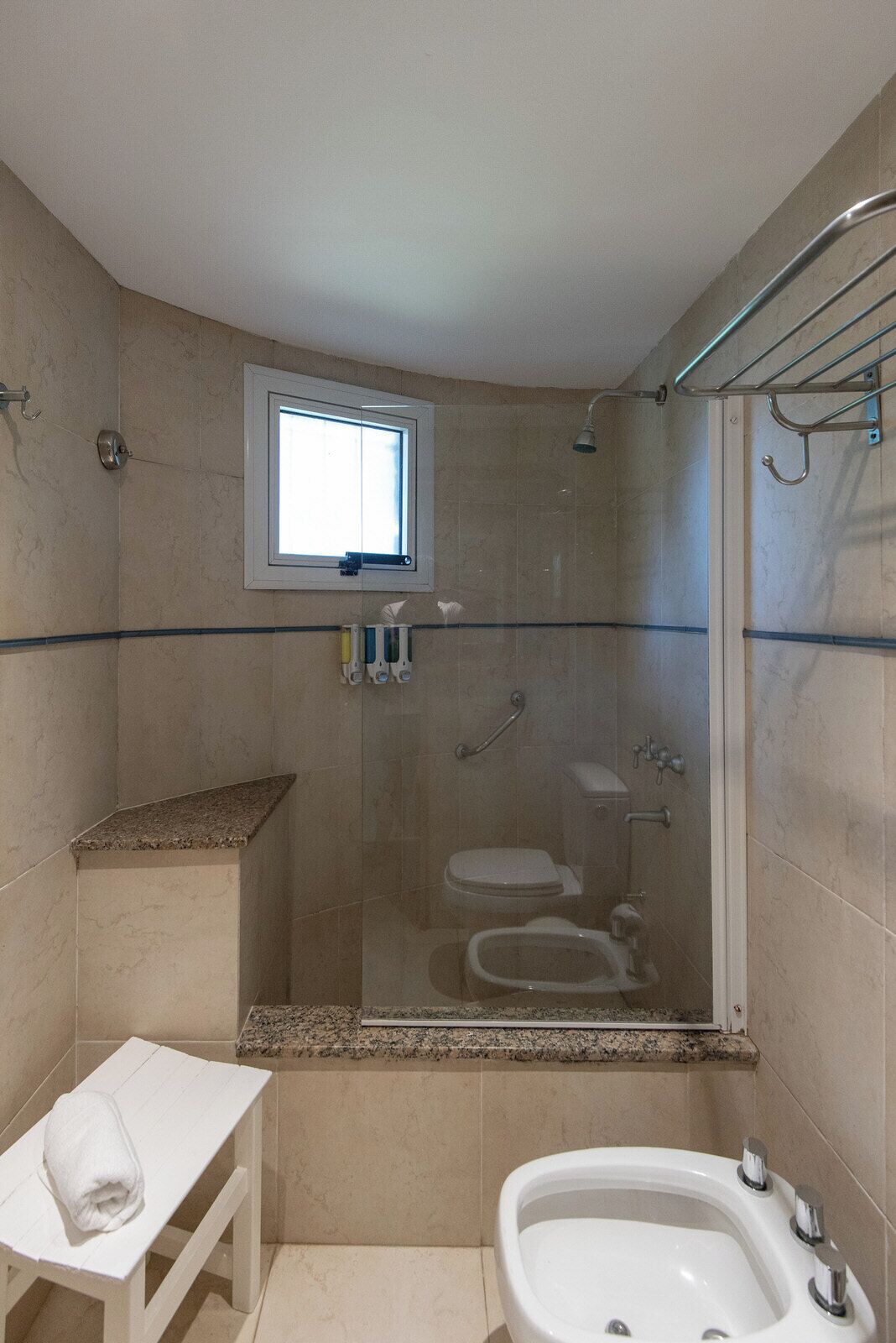 A bathroom with a shower, toilet, bidet, and a small window.