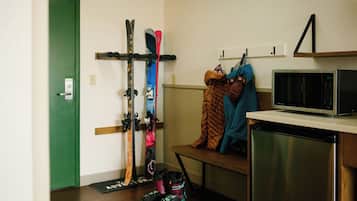 A room with a green door, skis and ski boots on a rack, a microwave, and a dishwasher.