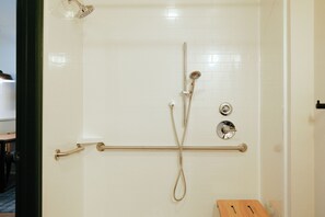 A shower area with a handheld showerhead, a wall-mounted faucet, and a grab bar. - White Pine Adventure Inn (Pinedale)