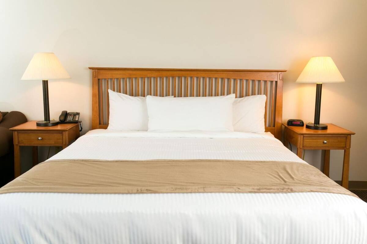 A neatly made bed with white linens and a wooden headboard, flanked by two bedside tables with lamps and clocks.