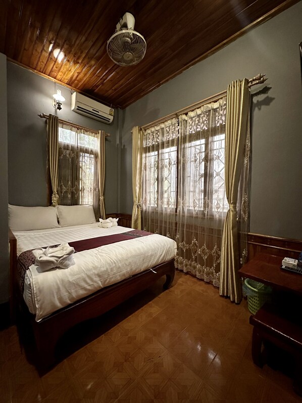 Een hotelkamer met een houten plafond, een bed met witte lakens, een houten bankje en een groene prullenbak.