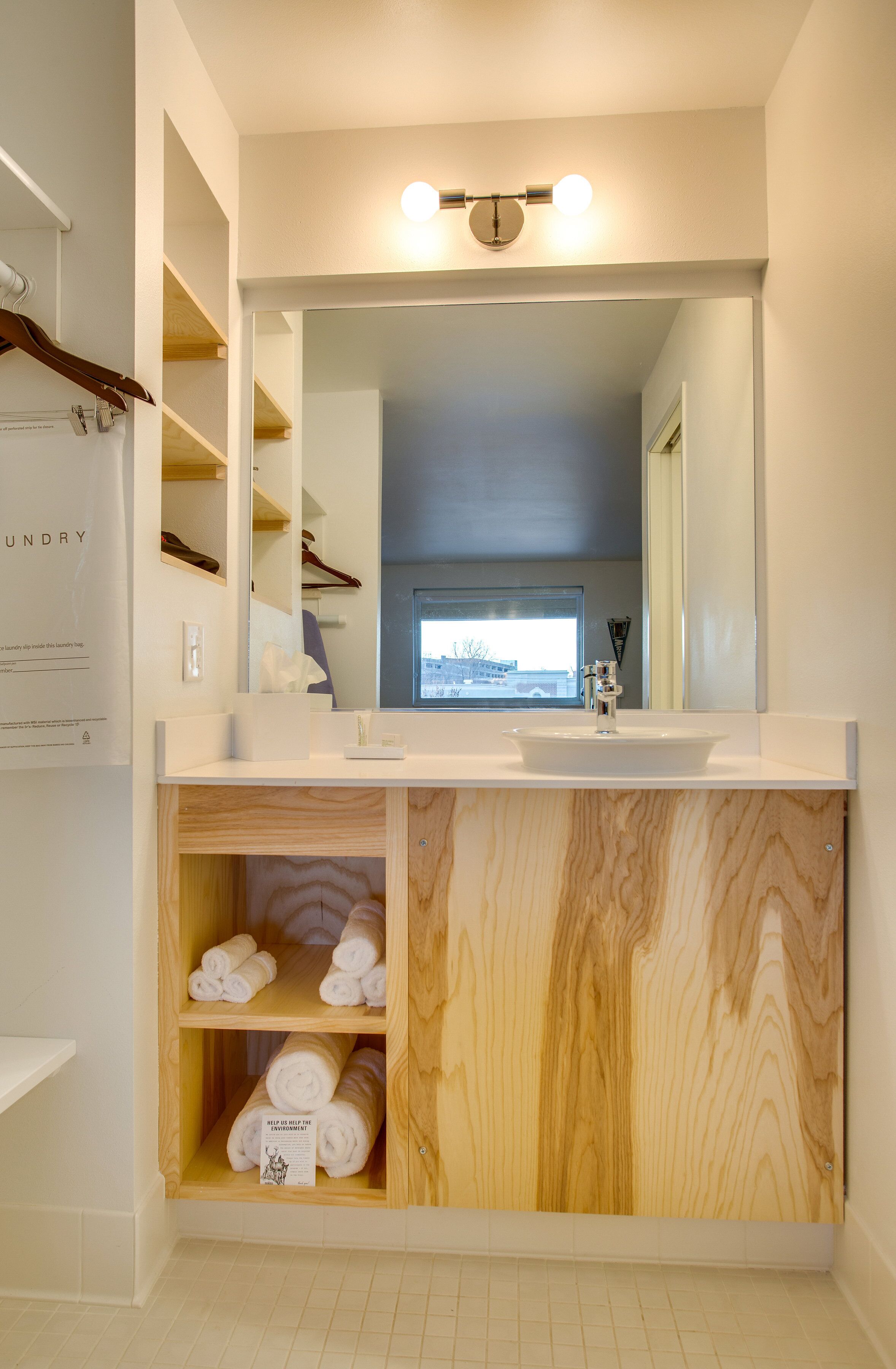 A modern bathroom with a large mirror, wooden shelves, and a view of the outside.