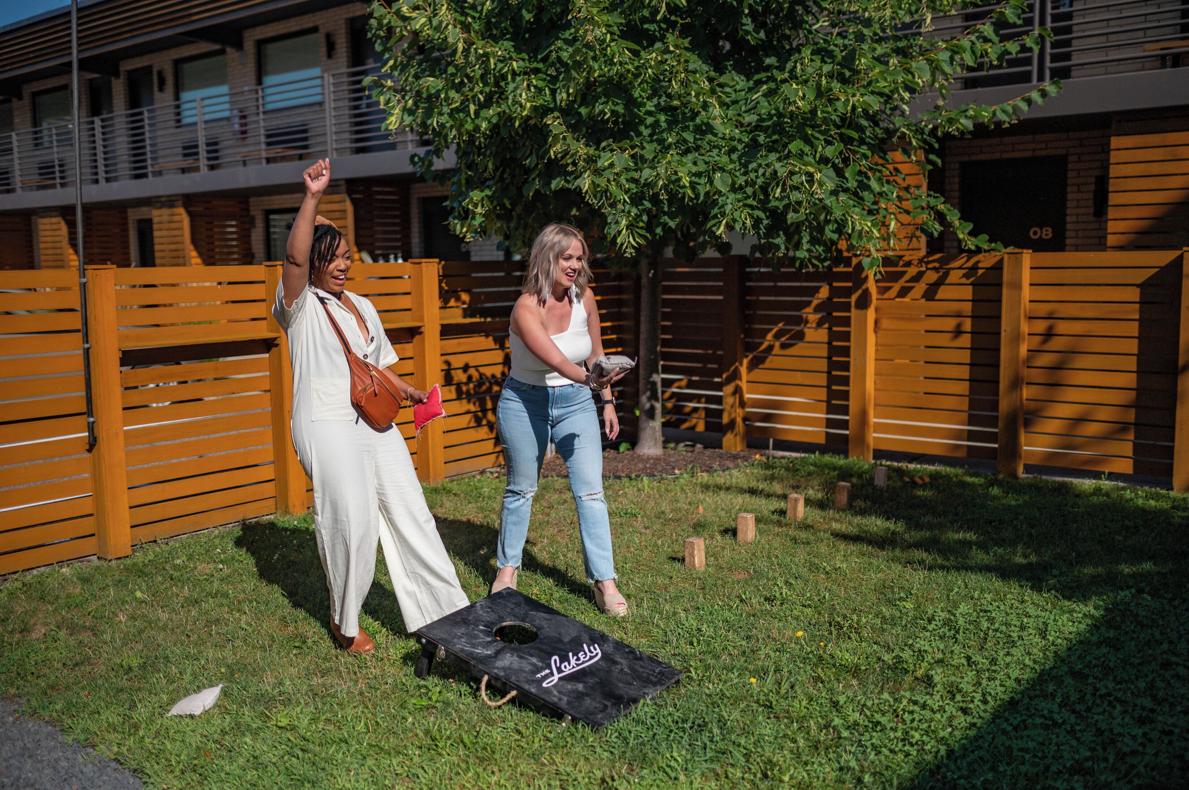 Two people playing a game outdoors with a bag labeled "Laksy" on the ground.