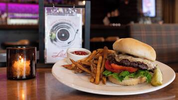 A burger with fries and ketchup on a plate, a candle, and a menu in the background.