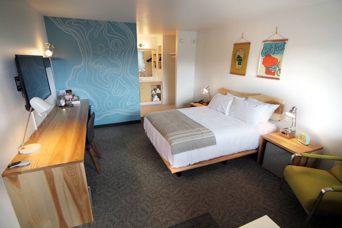 Una habitación de hotel con cama, mesita de noche, silla, escritorio y espejo.