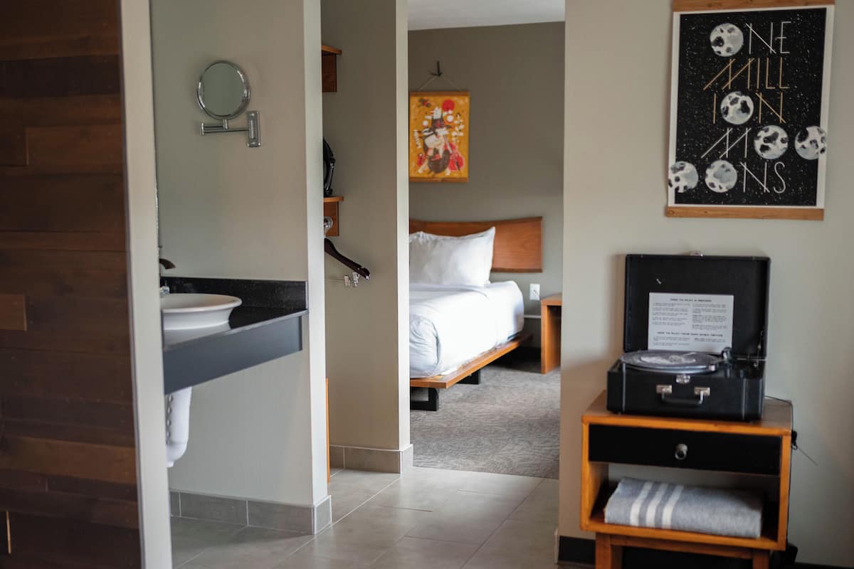 Habitación de hotel con baño, cama, mesita de noche con tocadiscos y un cartel en la pared.