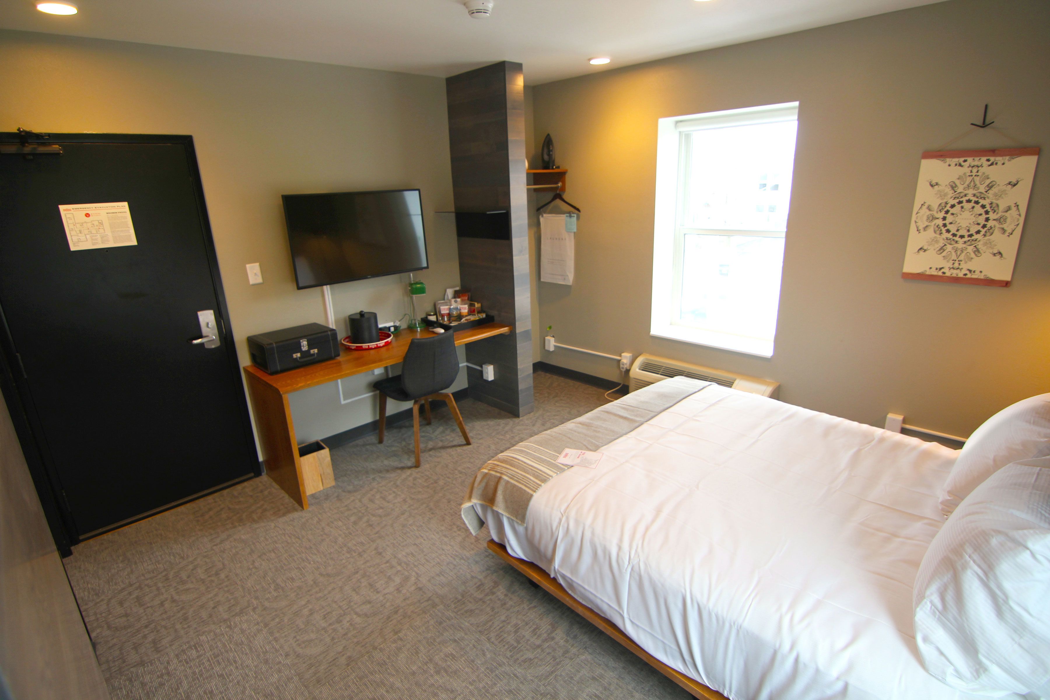 A hotel room with a bed, a desk with a chair, a television, and a window.