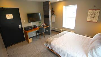 A hotel room with a bed, a desk with a chair, a television, and a window.