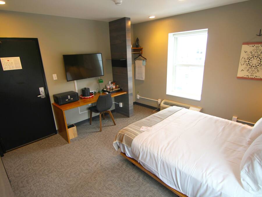 A hotel room with a bed, a desk with a chair, a television, and a window.