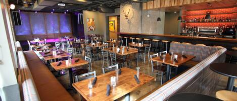 A restaurant with multiple tables and booths, a bar area, and a wall-mounted clock.