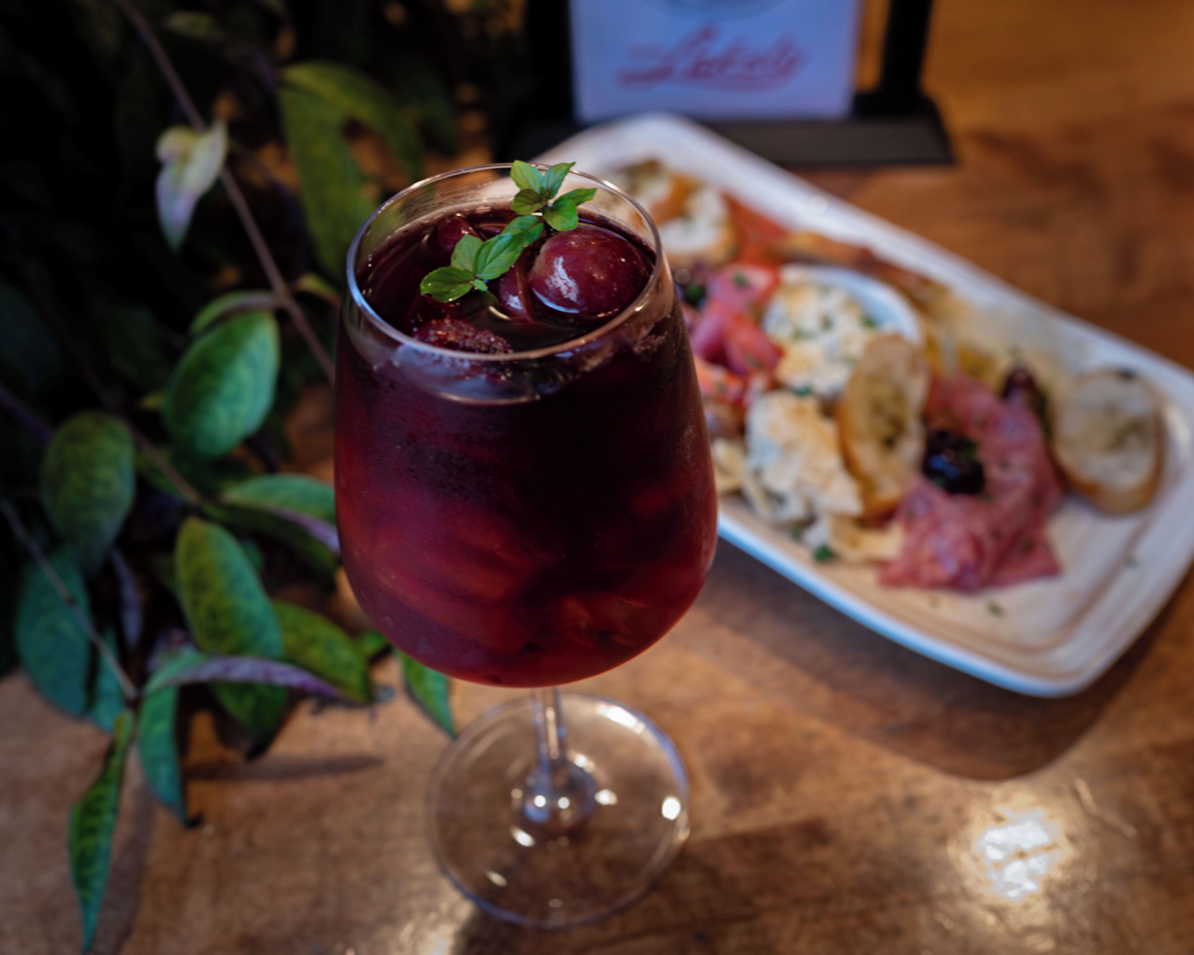 A glass of red beverage with a mint garnish on a wooden table.