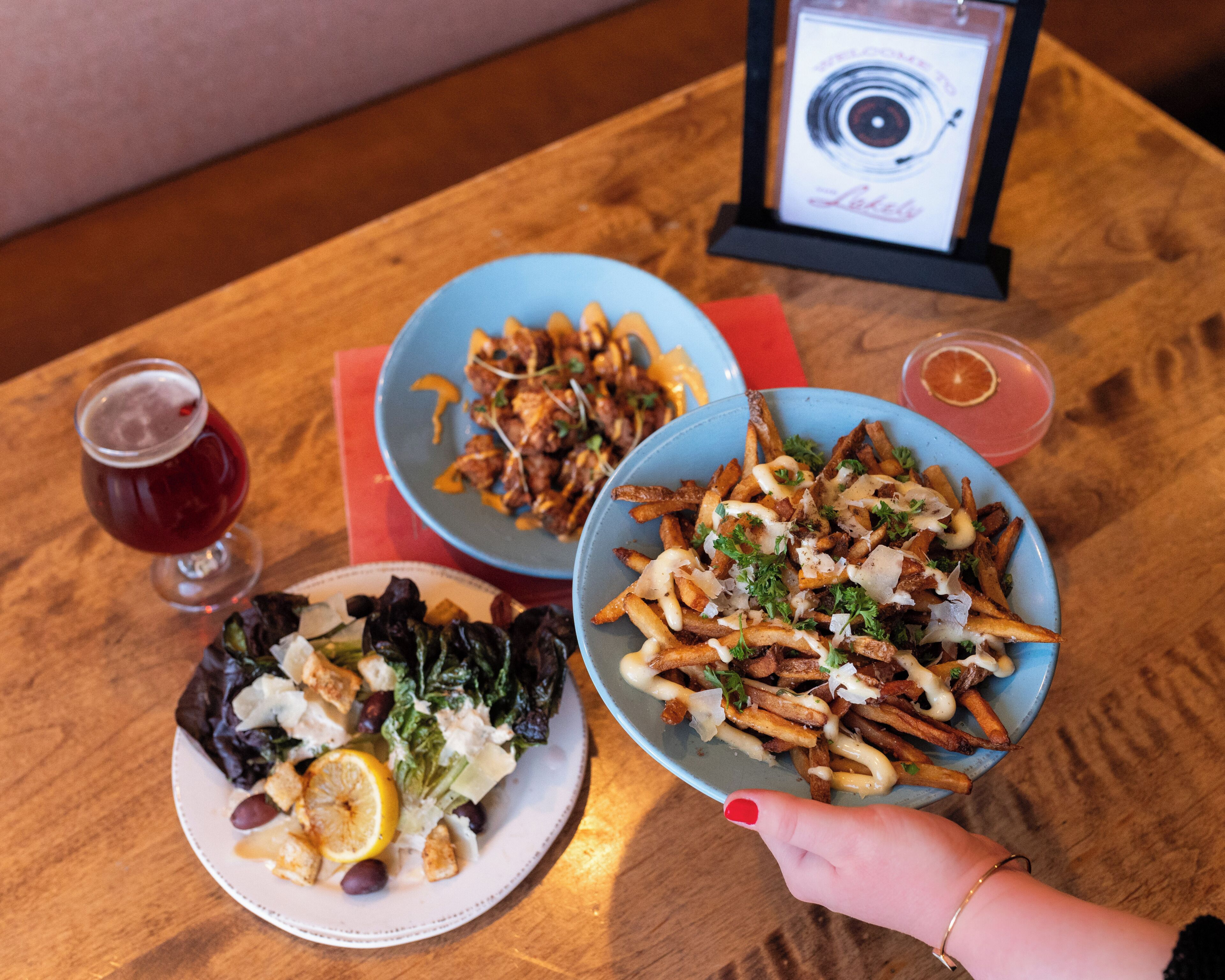 A table with three plates of food, a drink, and a framed welcome sign.