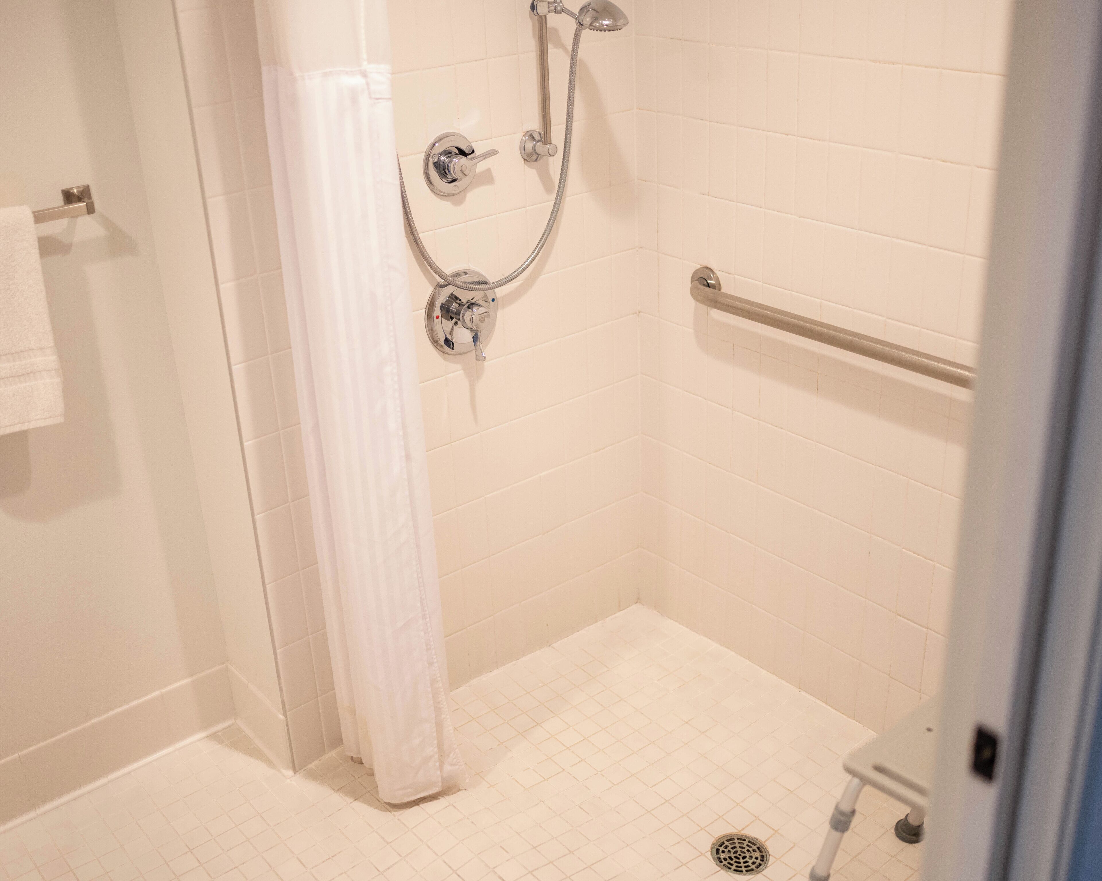 Un área de ducha pequeña con azulejos blancos y un cabezal de ducha y grifo de mano.