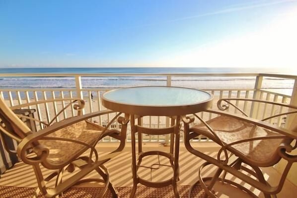 A balcony with a glass table and metal chairs overlooking a beach.