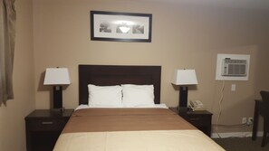 A hotel room with a bed, two bedside tables with lamps, a framed picture on the wall, and an air conditioning unit. - Sunrise Motel (Regina)