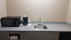 Una kitchenette con microondas, cafetera y lavamanos.