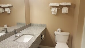 A bathroom with a granite countertop sink, a mirror, a toilet, and a towel rack with towels. - Sunrise Motel (Regina)