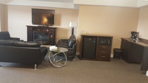 Habitación de hotel con televisor de pantalla plana, sofá de cuero, sillón, una mesita redonda, minibar y escritorio con lámpara.