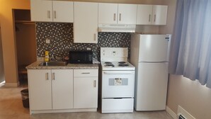 Una cocina compacta con armarios blancos, un microondas, una estufa y un refrigerador.
