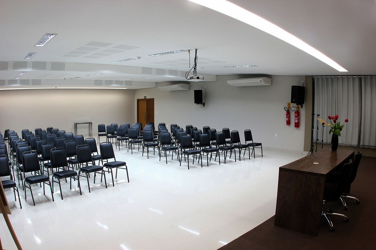 A conference room with rows of chairs, a podium, and a projector on the ceiling.