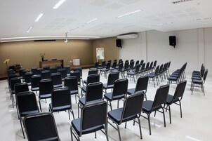 Un salón de conferencias con filas de sillas negras, un atril, una pizarra y un altavoz en la pared.