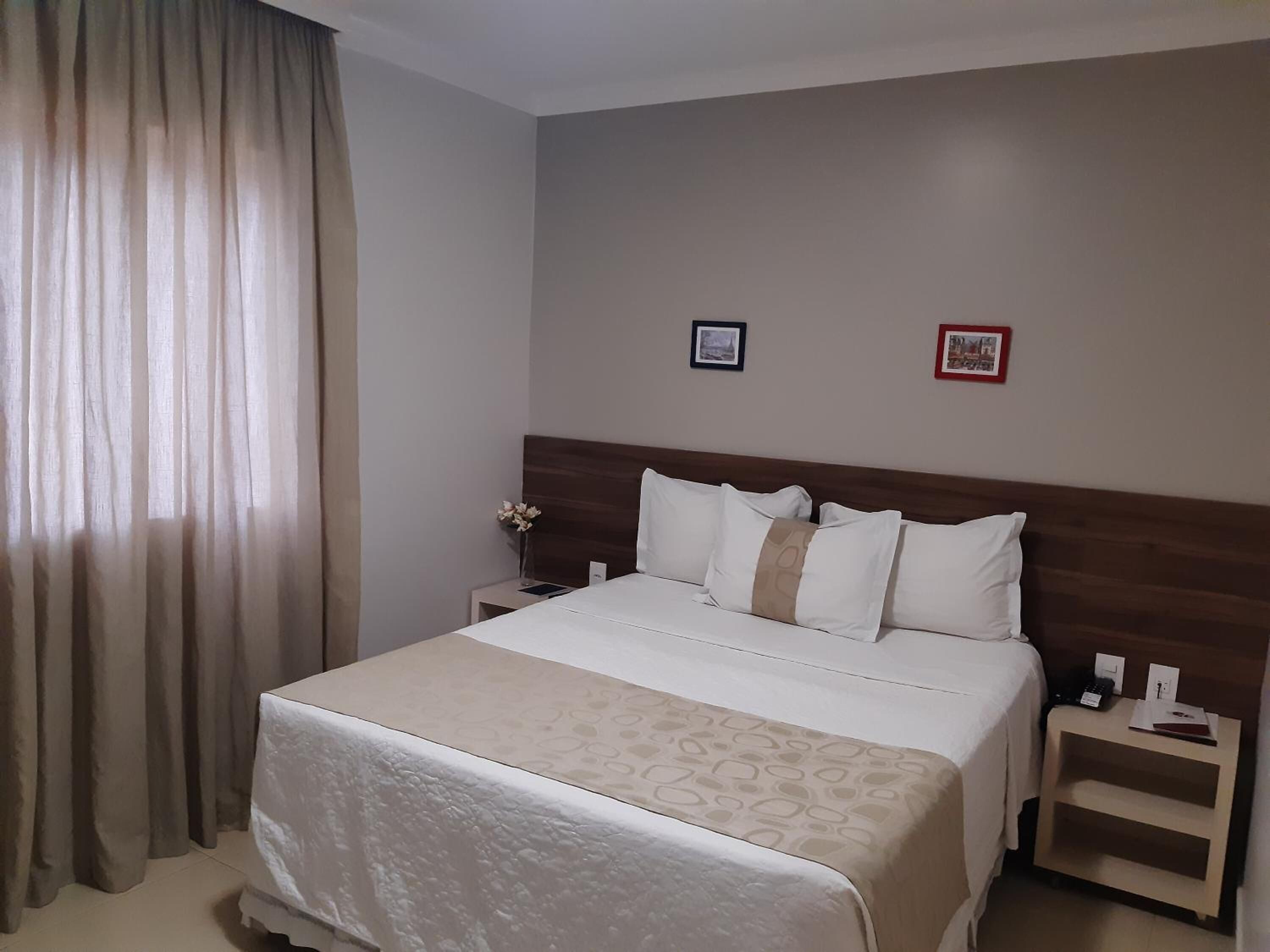 A hotel room with a large bed, a wooden headboard, two bedside tables, and a nightstand.