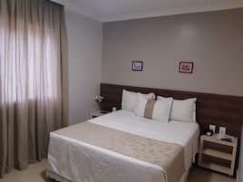 A hotel room with a large bed, a wooden headboard, two bedside tables, and a nightstand.