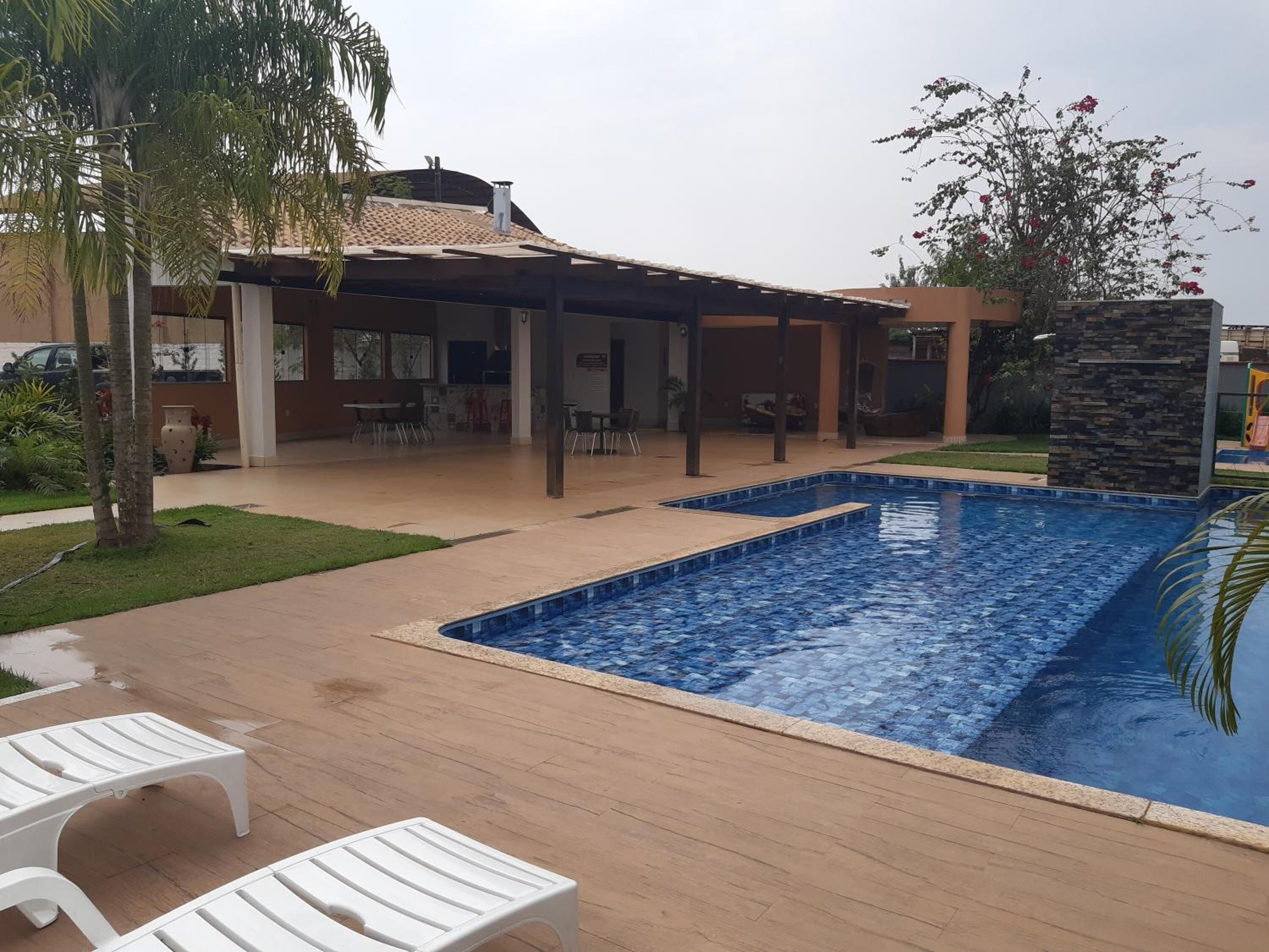 A swimming pool with a tiled deck, outdoor seating, and a covered patio area.