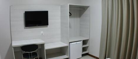 A compact hotel room with a bed, a desk with a chair, a TV, a wardrobe, and a small refrigerator.