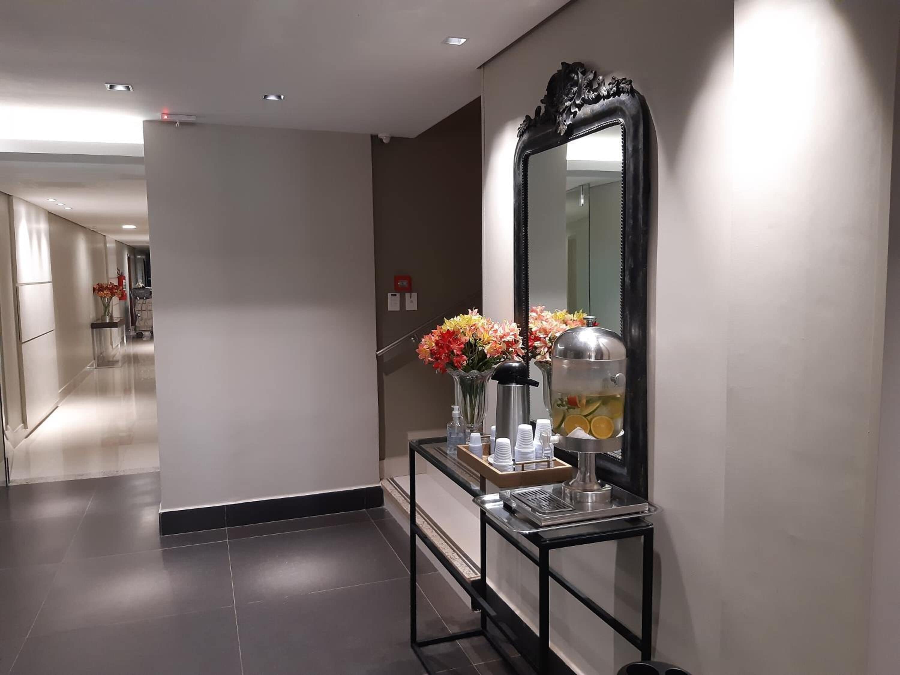 A hallway with a black-framed mirror, a small table with a water dispenser, and vases with flowers.