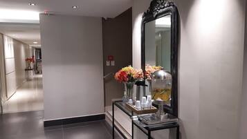 A hallway with a black-framed mirror, a small table with a water dispenser, and vases with flowers.