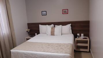 A hotel room with a bed, two bedside tables, a nightstand, a lamp, and two framed pictures on the wall.