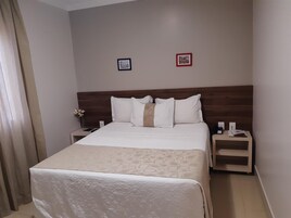 Habitación de hotel con una cama, dos mesitas de noche, una lámpara y dos cuadros en la pared.