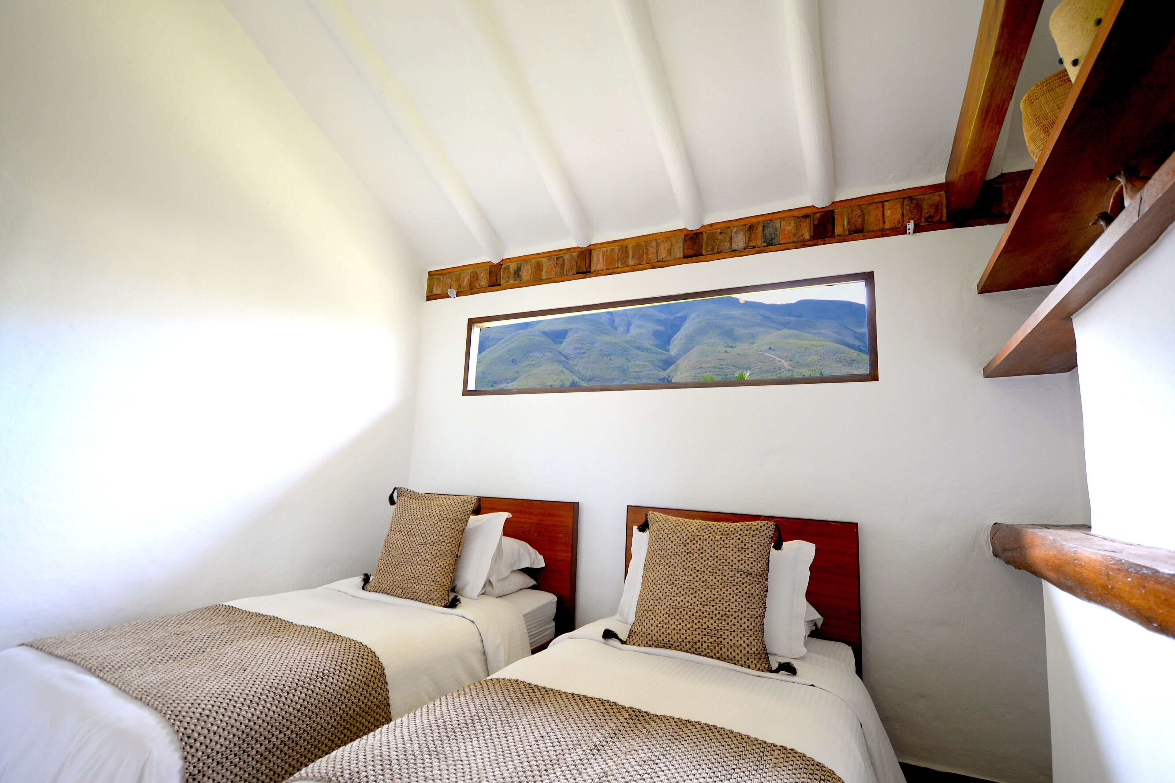 Una habitación con dos camas, cabeceros de madera, un ventanal con vistas a la montaña y una viga de madera en el techo.