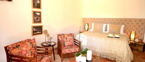 A room with a bed, two chairs, a small table, and a decorative vase.