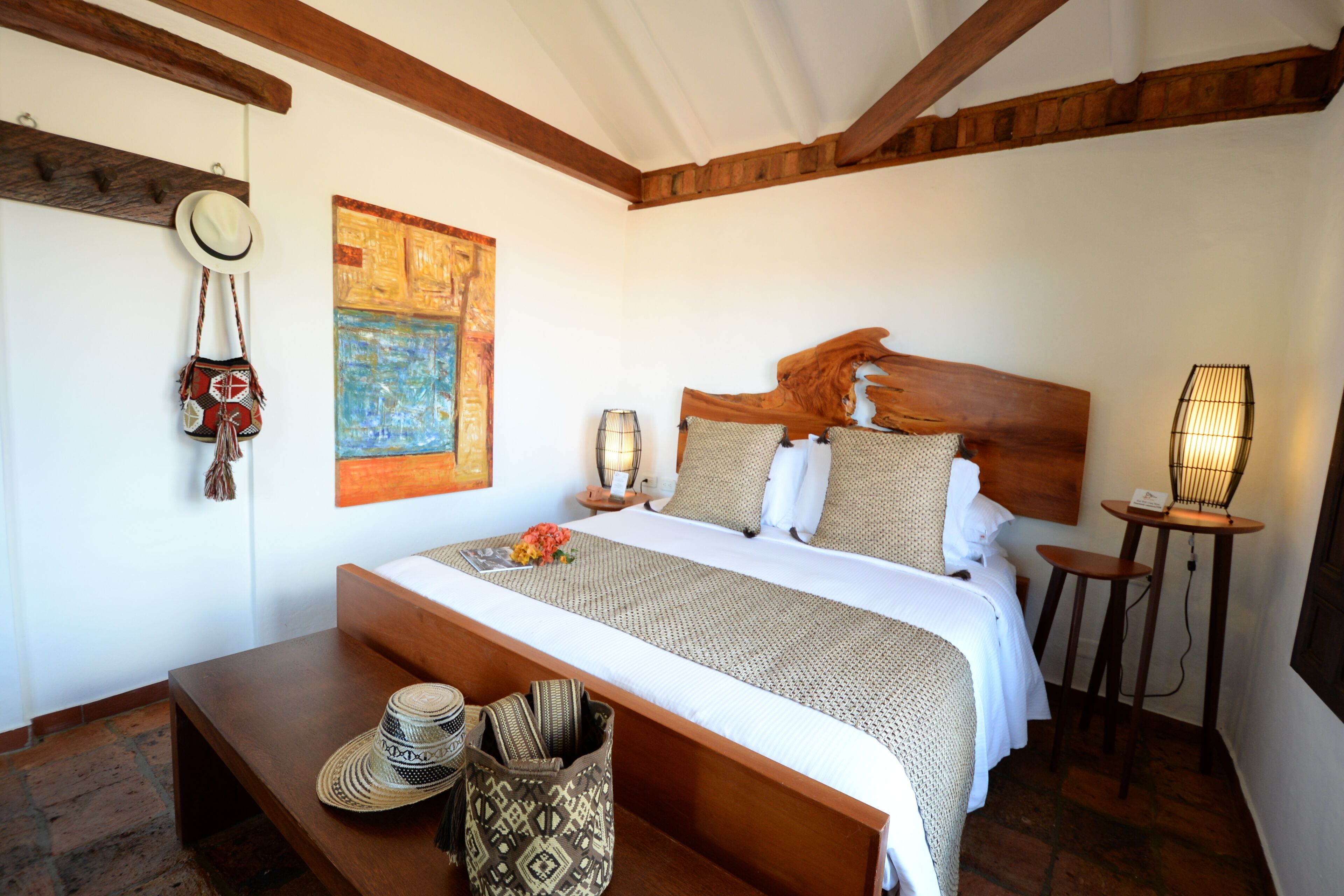 Un dormitorio con cabecera de madera, una cama grande, una mesita de noche con lámpara y un perchero en la pared.