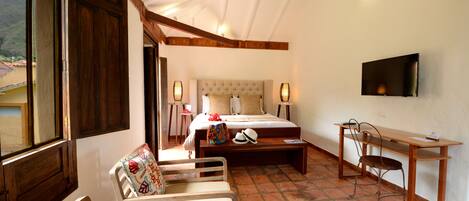 A bedroom with a bed, bedside table, chair, desk, and TV.