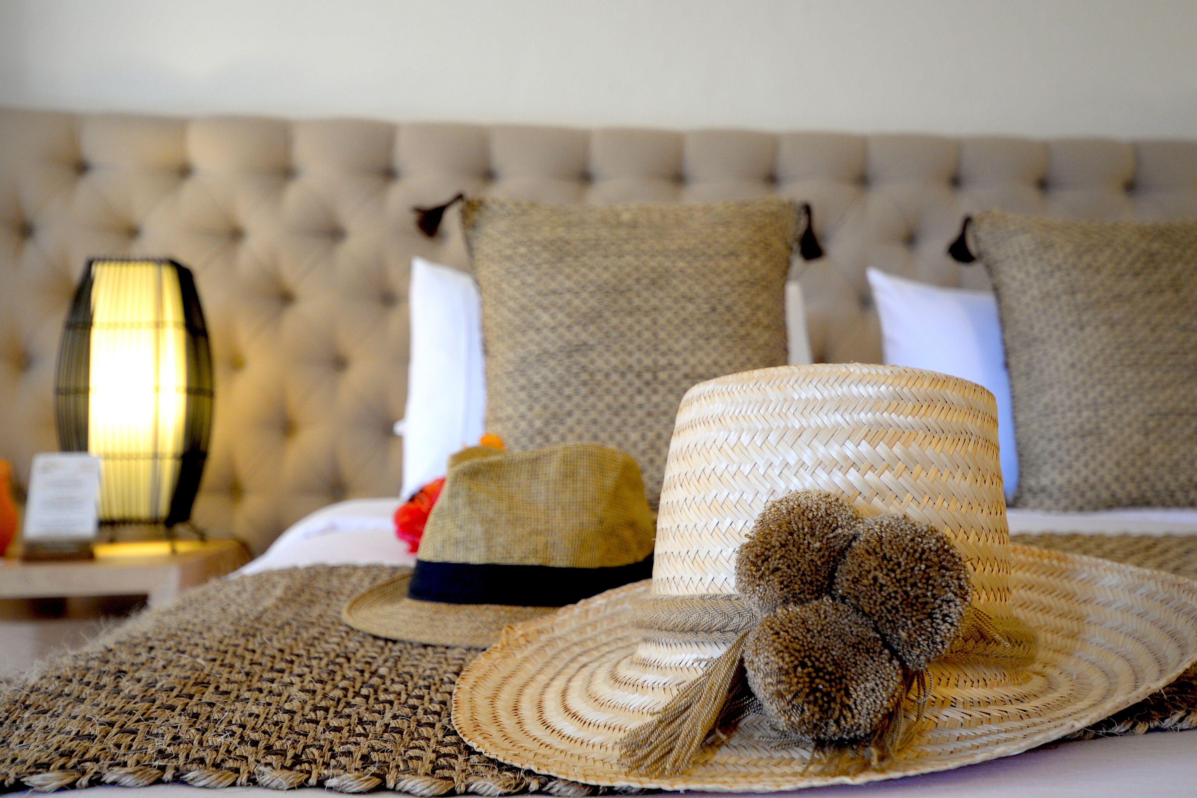 A bed with a tufted headboard, a woven blanket, and several straw hats.