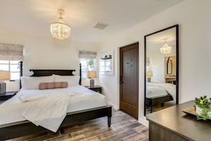 A bedroom with a large bed, a wooden headboard, a chandelier, a mirror, and a bedside table with a lamp.